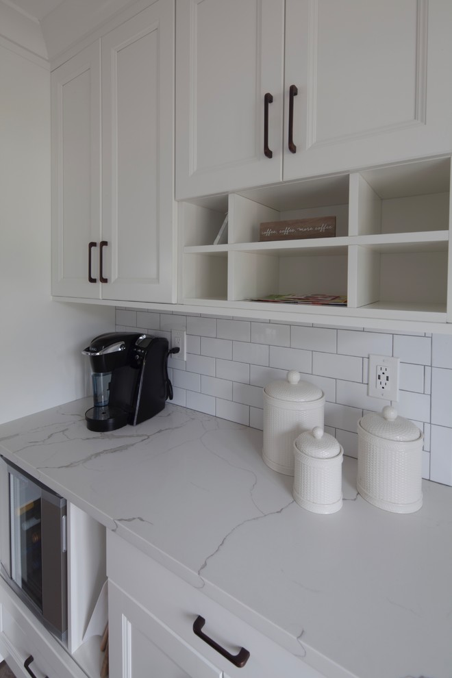 Foto på ett mellanstort funkis vit kök, med en undermonterad diskho, skåp i shakerstil, vita skåp, marmorbänkskiva, vitt stänkskydd, stänkskydd i tunnelbanekakel, rostfria vitvaror, mörkt trägolv, en köksö och brunt golv