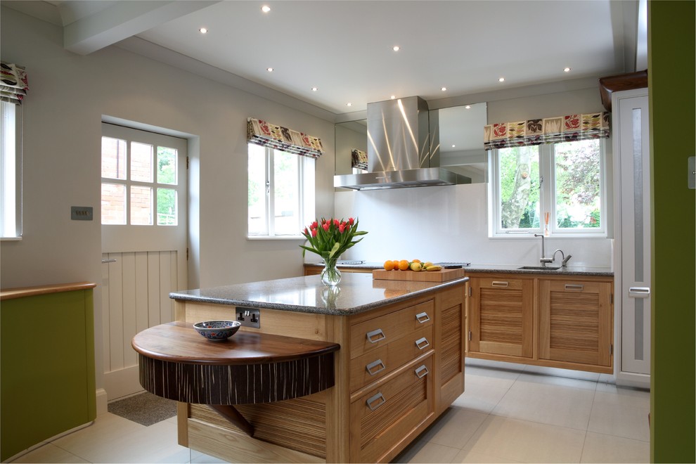 Bild på ett mellanstort funkis kök, med luckor med upphöjd panel, skåp i ljust trä, granitbänkskiva, rostfria vitvaror, kalkstensgolv och en köksö
