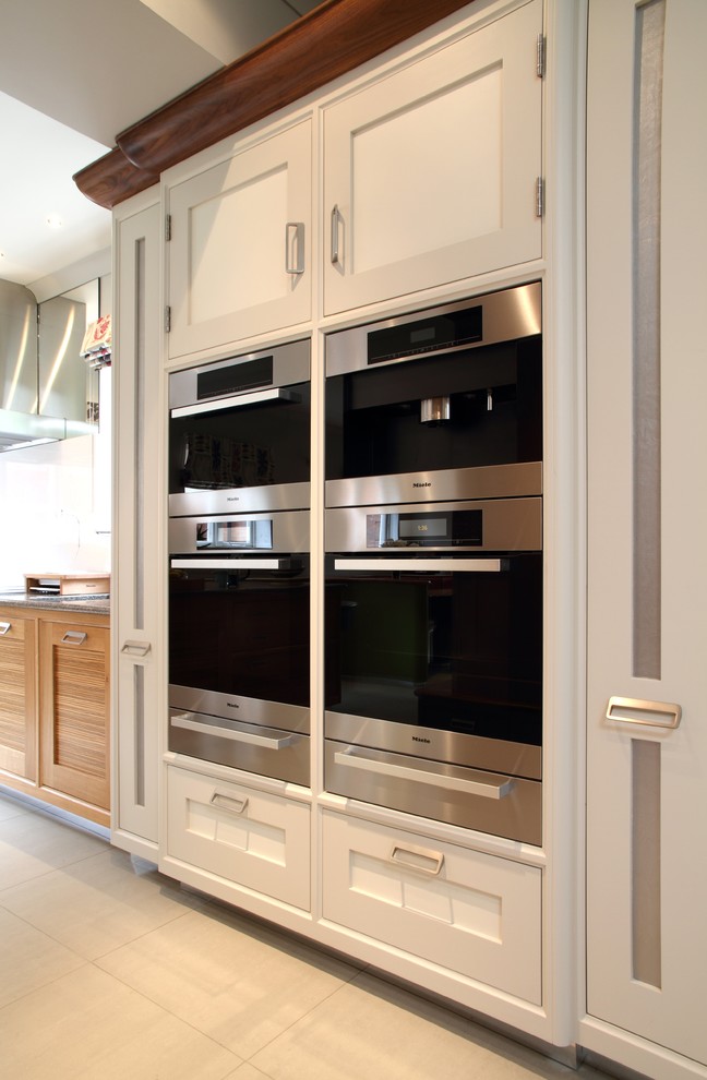 Immagine di una cucina design di medie dimensioni con ante con bugna sagomata, ante in legno chiaro, top in granito, elettrodomestici in acciaio inossidabile e pavimento in pietra calcarea