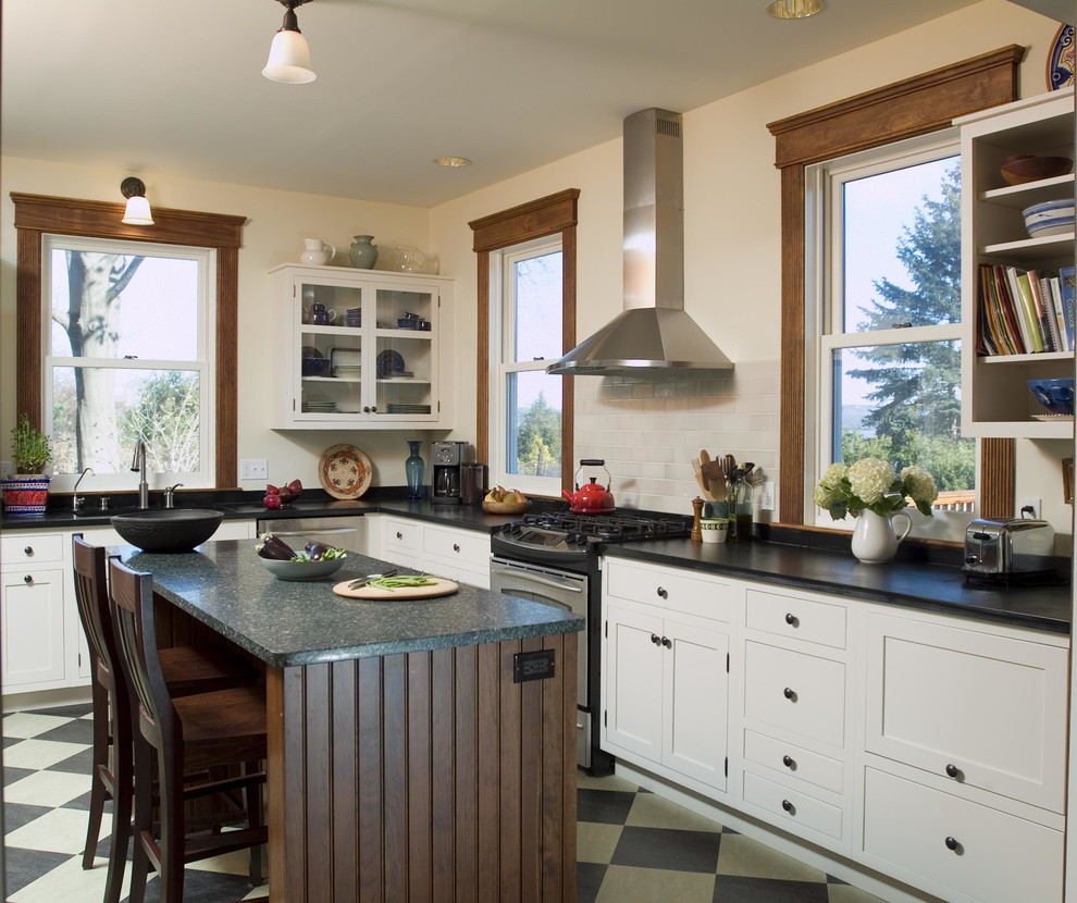 Photo of a large rural l-shaped kitchen/diner in New York with a double-bowl sink, shaker cabinets, white cabinets, soapstone worktops, stone slab splashback, stainless steel appliances, lino flooring, an island, white splashback, multi-coloured floors and black worktops.
