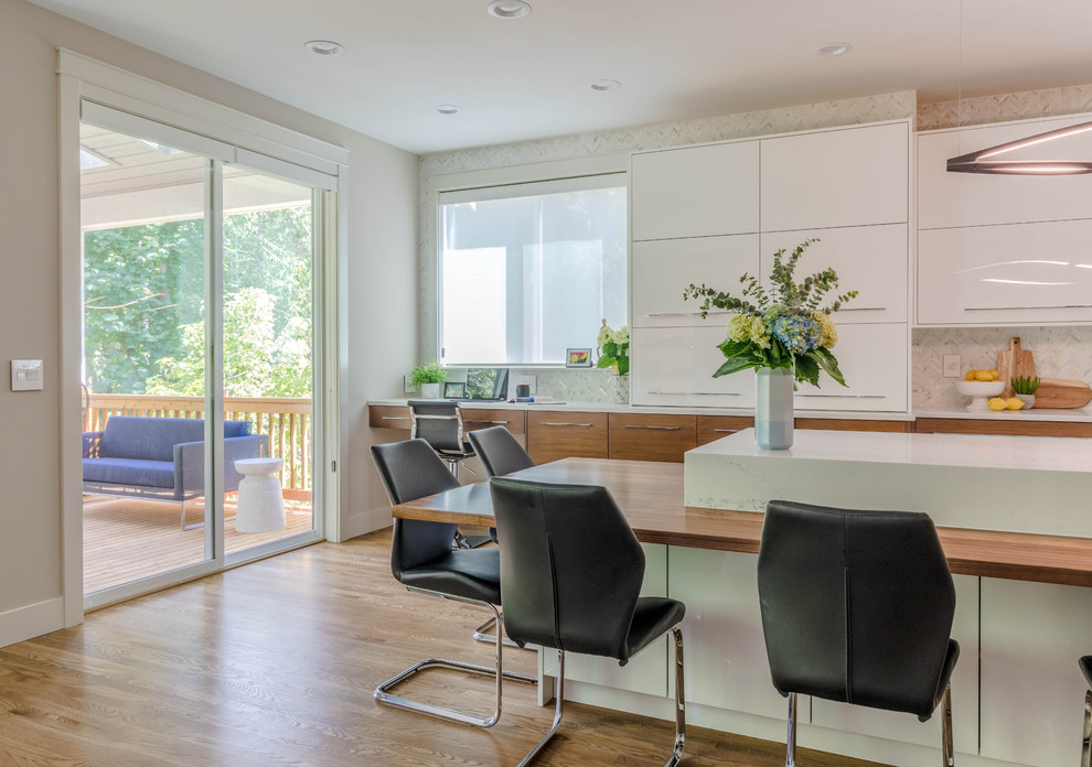 This is an example of an expansive classic l-shaped open plan kitchen in Seattle with a submerged sink, flat-panel cabinets, light wood cabinets, marble worktops, white splashback, marble splashback, stainless steel appliances, light hardwood flooring, an island, brown floors and white worktops.