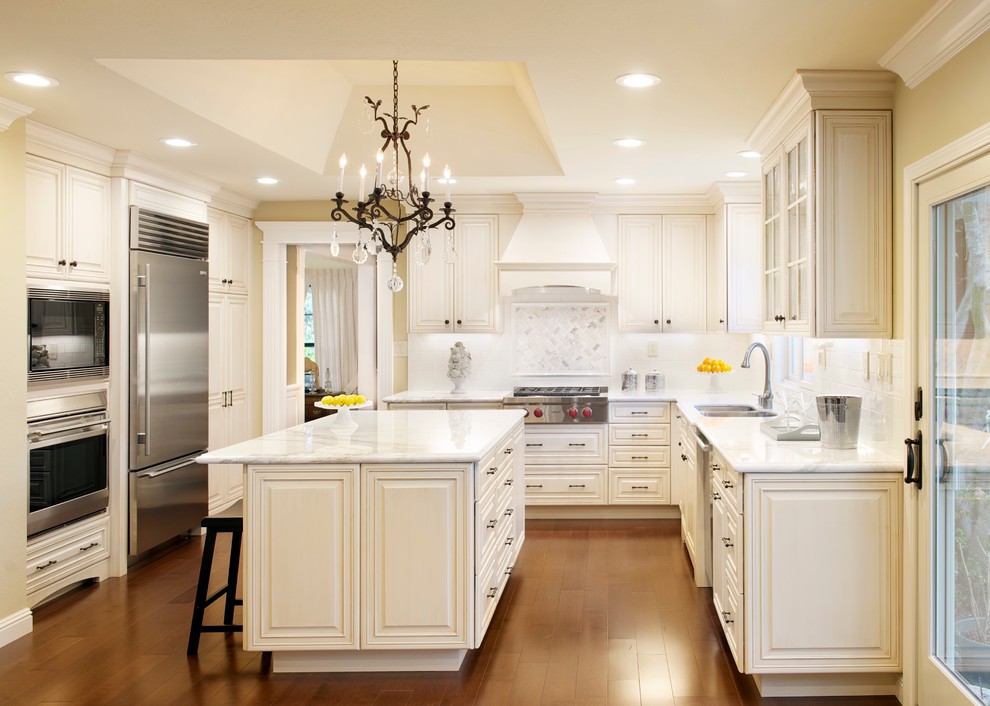 Elegant u-shaped kitchen photo in San Francisco with a double-bowl sink, raised-panel cabinets, white cabinets, white backsplash and stainless steel appliances