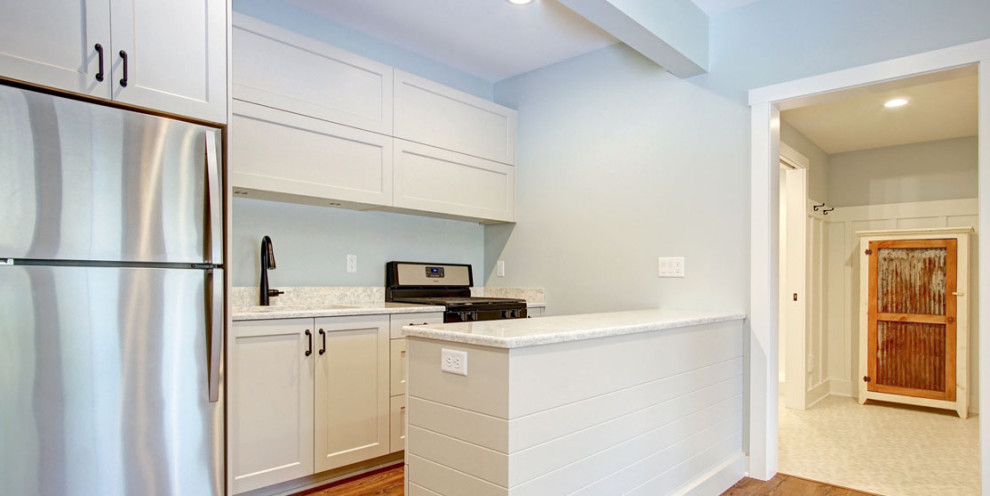 Bild på ett avskilt, litet vit linjärt vitt kök, med en undermonterad diskho, luckor med infälld panel, vita skåp, bänkskiva i kvarts, svarta vitvaror, mellanmörkt trägolv och brunt golv
