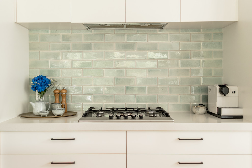 Photo of a small contemporary galley kitchen/diner in Auckland with a double-bowl sink, flat-panel cabinets, white cabinets, marble worktops, green splashback, metro tiled splashback, stainless steel appliances, medium hardwood flooring, an island and brown floors.