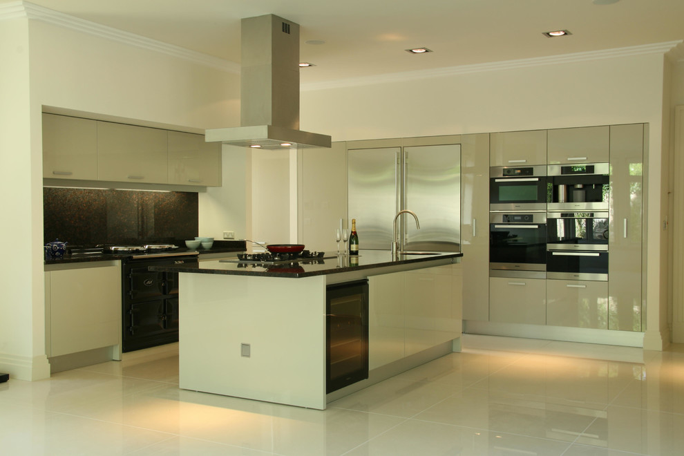 This is an example of a contemporary l-shaped kitchen/diner in Dublin with flat-panel cabinets, beige cabinets, granite worktops, brown splashback, stone slab splashback, stainless steel appliances and an island.
