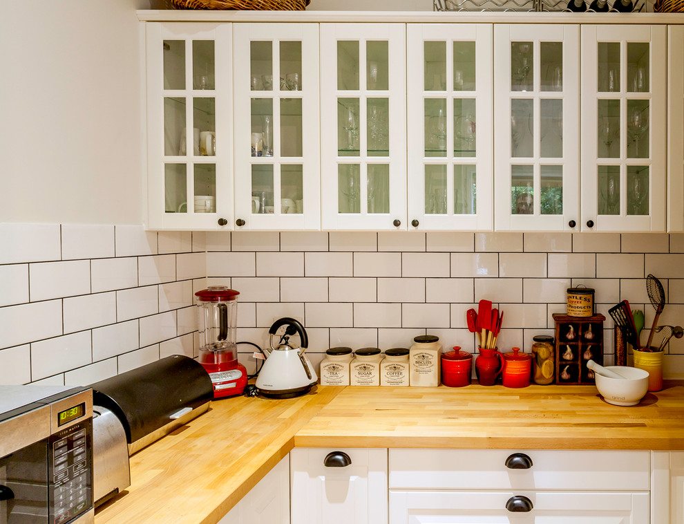 Bild på ett funkis kök, med träbänkskiva, vitt stänkskydd, stänkskydd i tunnelbanekakel, luckor med infälld panel, vita skåp och mellanmörkt trägolv