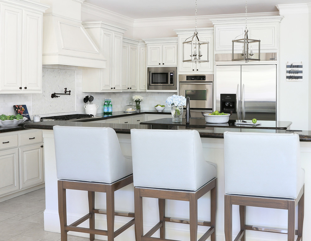 Inspiration for a medium sized coastal l-shaped kitchen/diner in Houston with a built-in sink, raised-panel cabinets, white cabinets, granite worktops, white splashback, marble splashback, stainless steel appliances, travertine flooring, an island and beige floors.