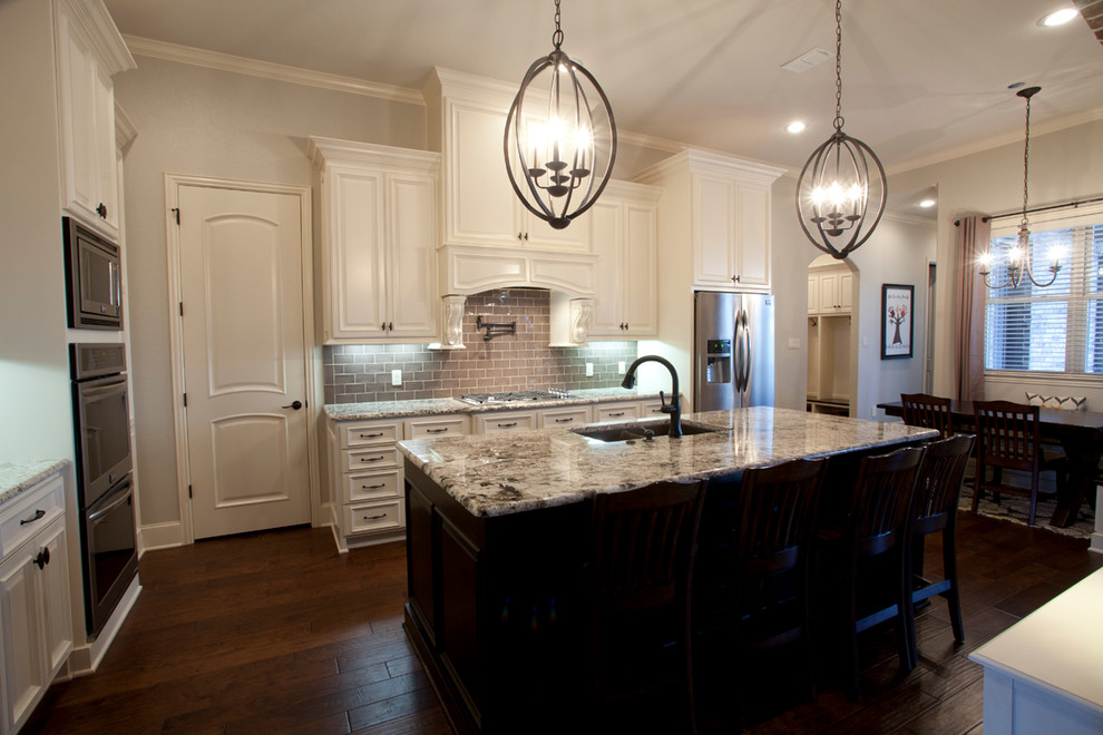 Klassisk inredning av ett mellanstort kök, med en dubbel diskho, luckor med upphöjd panel, vita skåp, granitbänkskiva, brunt stänkskydd, stänkskydd i glaskakel, rostfria vitvaror, mörkt trägolv och en köksö