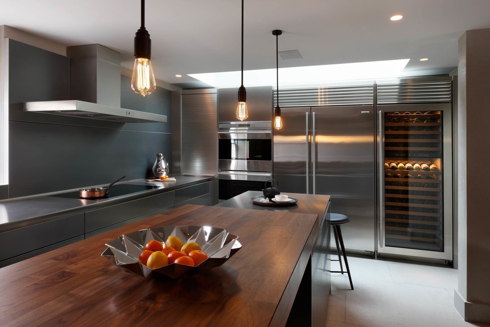 Foto på ett mellanstort funkis kök, med en integrerad diskho, släta luckor, skåp i rostfritt stål, bänkskiva i rostfritt stål, stänkskydd med metallisk yta, rostfria vitvaror, kalkstensgolv och en köksö