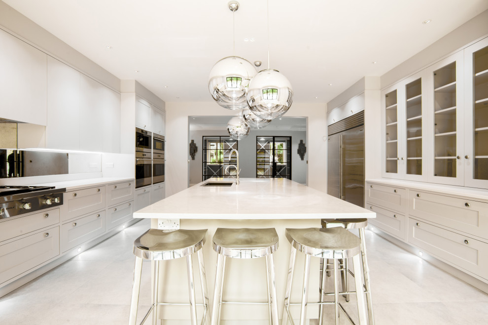Photo of a medium sized contemporary galley open plan kitchen in Berkshire with a built-in sink, glass-front cabinets, white cabinets, stainless steel appliances, a breakfast bar, white floors, white worktops and feature lighting.