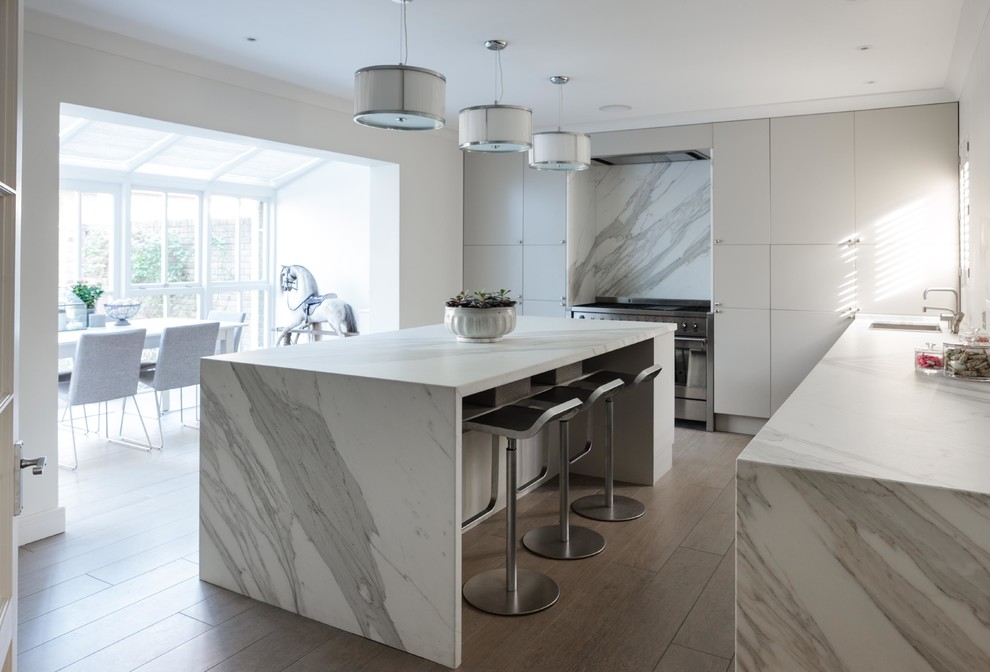 This is an example of a contemporary l-shaped kitchen/diner in London with flat-panel cabinets, white cabinets, stainless steel appliances and an island.
