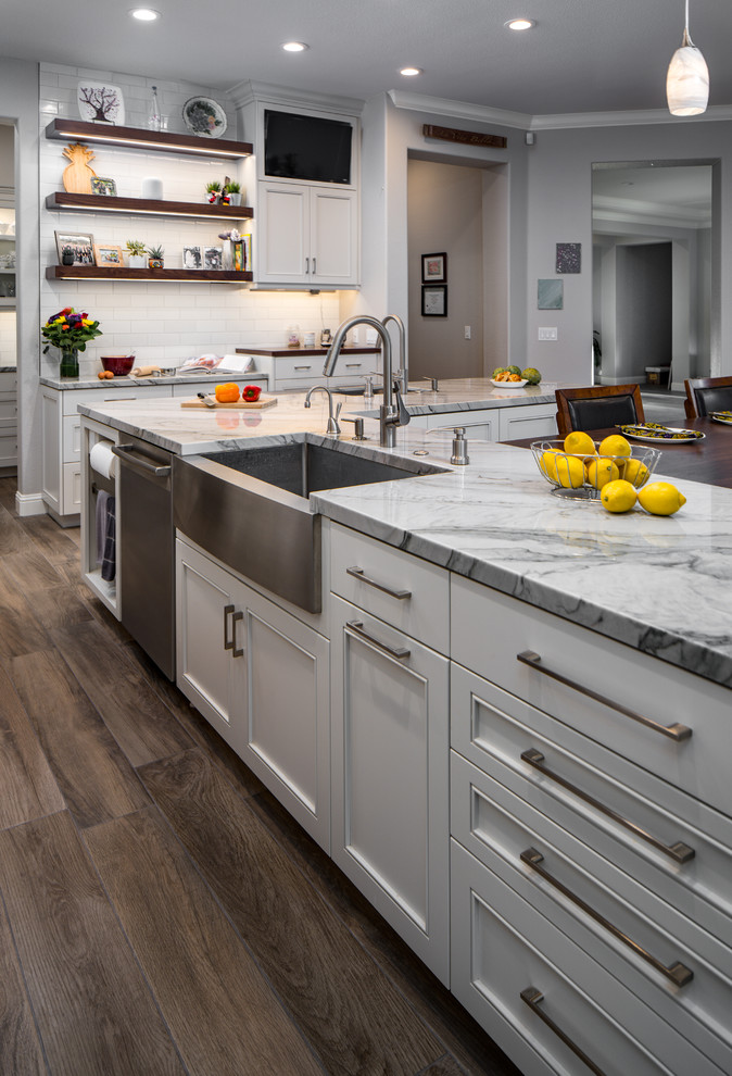 Inspiration for a large transitional l-shaped porcelain tile eat-in kitchen remodel in Sacramento with a farmhouse sink, recessed-panel cabinets, white cabinets, quartzite countertops, white backsplash, subway tile backsplash, stainless steel appliances, an island and white countertops