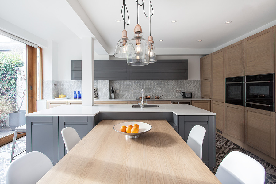 Large urban l-shaped ceramic tile eat-in kitchen photo in London with shaker cabinets, light wood cabinets, quartzite countertops, gray backsplash, stone tile backsplash, paneled appliances, an island and an undermount sink