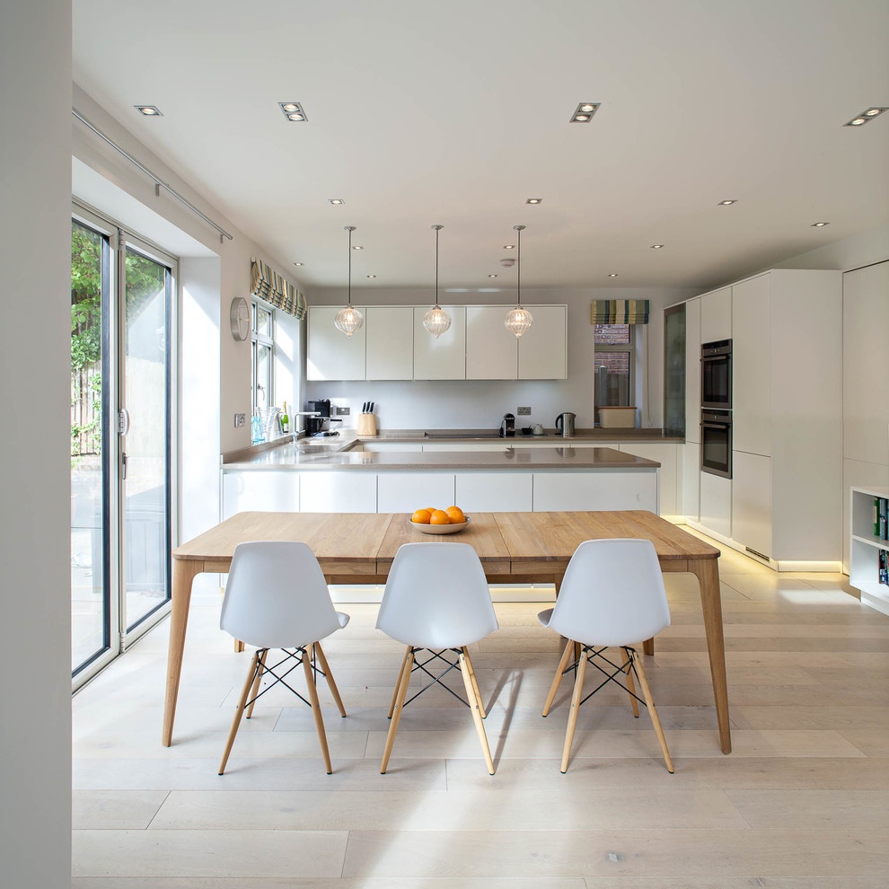 Große Nordische Wohnküche in U-Form mit flächenbündigen Schrankfronten, weißen Schränken, hellem Holzboden und Halbinsel in Hertfordshire