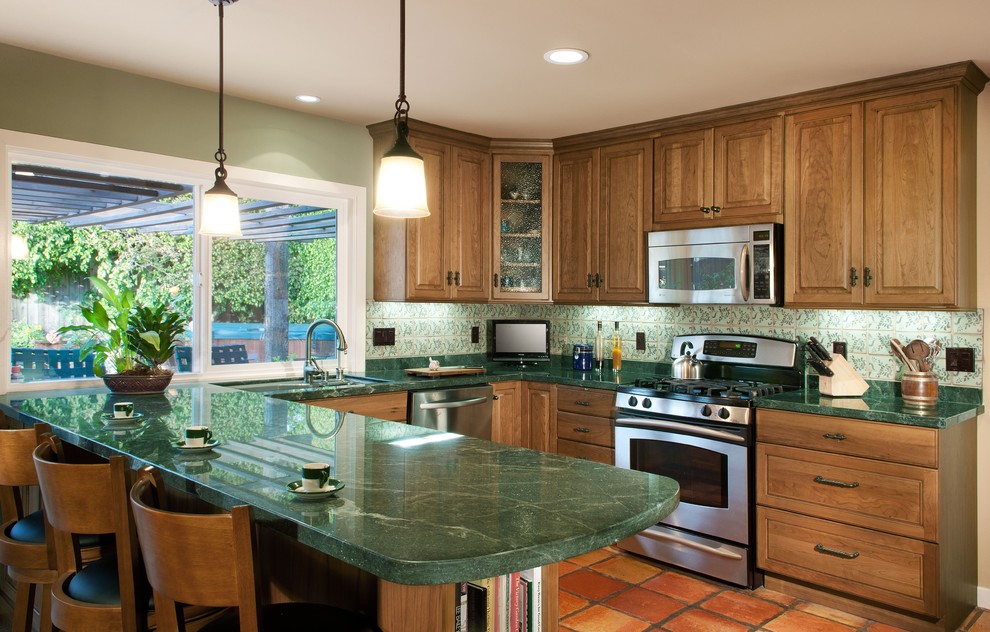 Exempel på ett mellanstort klassiskt kök, med en dubbel diskho, skåp i mellenmörkt trä, granitbänkskiva, grönt stänkskydd, stänkskydd i keramik, rostfria vitvaror och klinkergolv i terrakotta