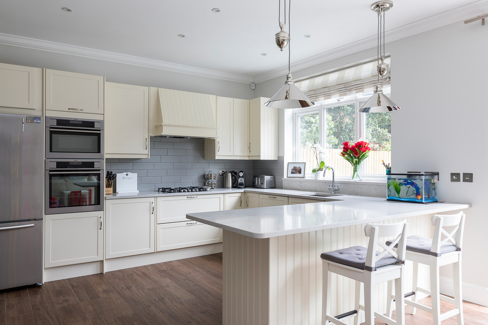 This is an example of a medium sized classic u-shaped open plan kitchen in London with a submerged sink, shaker cabinets, beige cabinets, granite worktops, grey splashback, porcelain splashback, stainless steel appliances, porcelain flooring, a breakfast bar and brown floors.