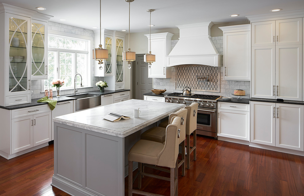 Inspiration for a large transitional medium tone wood floor eat-in kitchen remodel in New York with a farmhouse sink, recessed-panel cabinets, white cabinets, marble countertops, white backsplash, marble backsplash, stainless steel appliances and an island