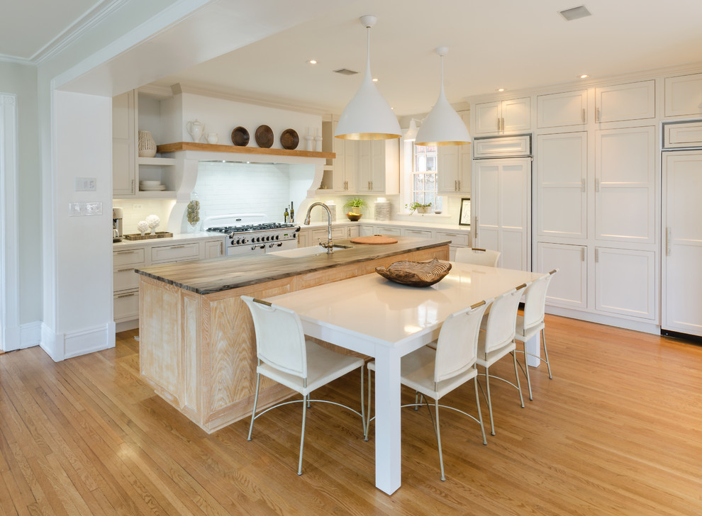 Example of a large transitional medium tone wood floor and brown floor kitchen design in Richmond with a farmhouse sink, shaker cabinets, white cabinets, quartzite countertops, white backsplash, ceramic backsplash, paneled appliances and an island