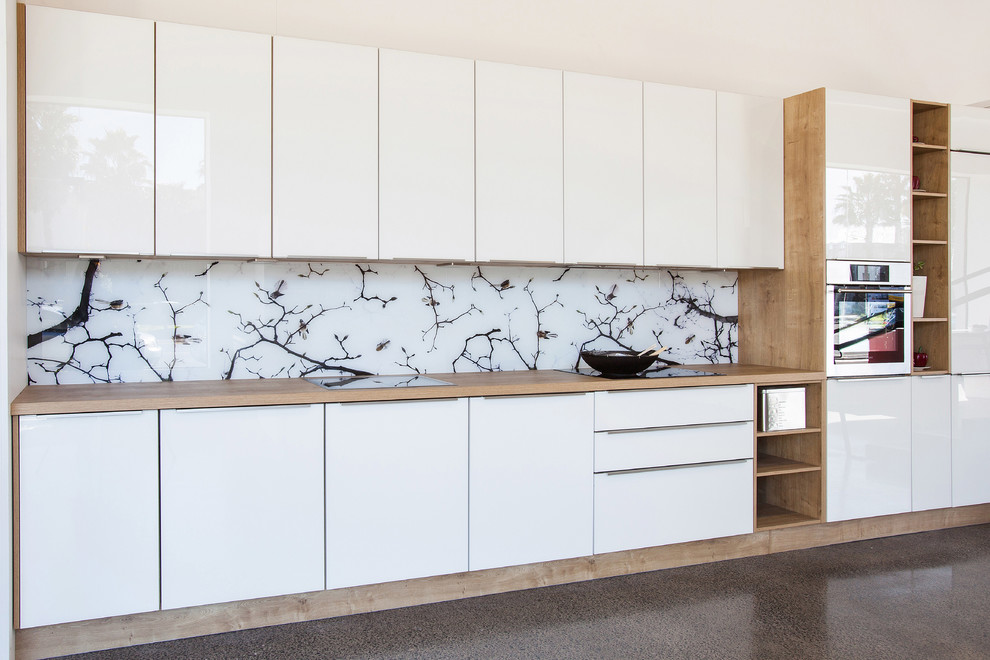 Inredning av ett minimalistiskt mellanstort kök, med träbänkskiva, vitt stänkskydd, glaspanel som stänkskydd, rostfria vitvaror och travertin golv
