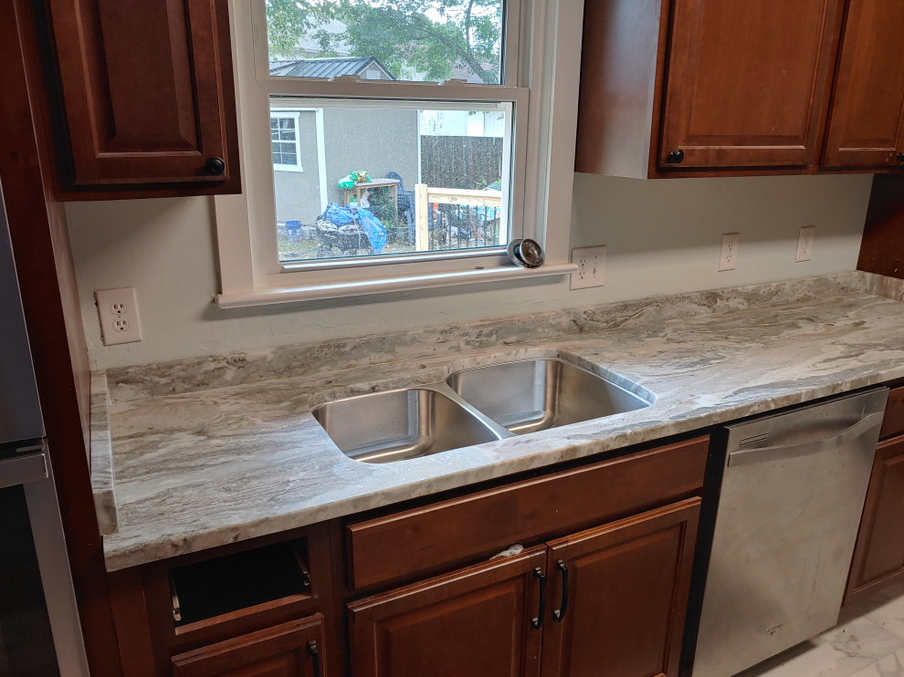 Inredning av ett grå grått kök och matrum, med en undermonterad diskho, bruna skåp, granitbänkskiva, grått stänkskydd och rostfria vitvaror
