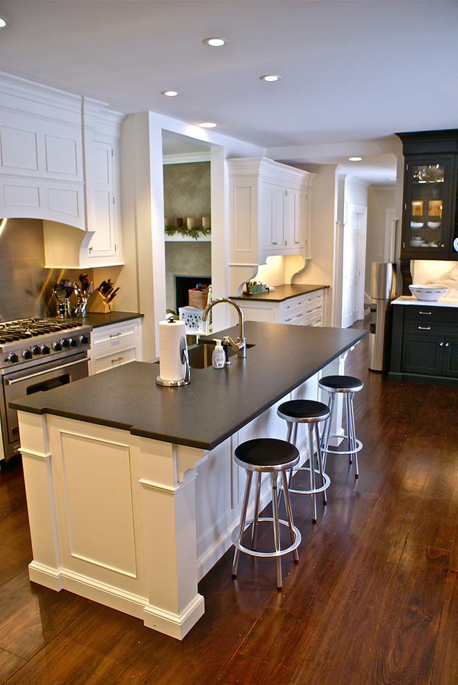 Klassisk inredning av ett stort kök och matrum, med en rustik diskho, luckor med profilerade fronter, vita skåp, granitbänkskiva, vitt stänkskydd, stänkskydd i stenkakel, rostfria vitvaror, mellanmörkt trägolv och en köksö