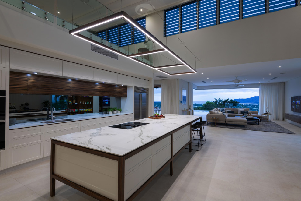 Photo of an expansive contemporary galley open plan kitchen in Cairns with a submerged sink, recessed-panel cabinets, white cabinets, engineered stone countertops, white splashback, mirror splashback, black appliances, porcelain flooring, an island, white floors, white worktops and a vaulted ceiling.