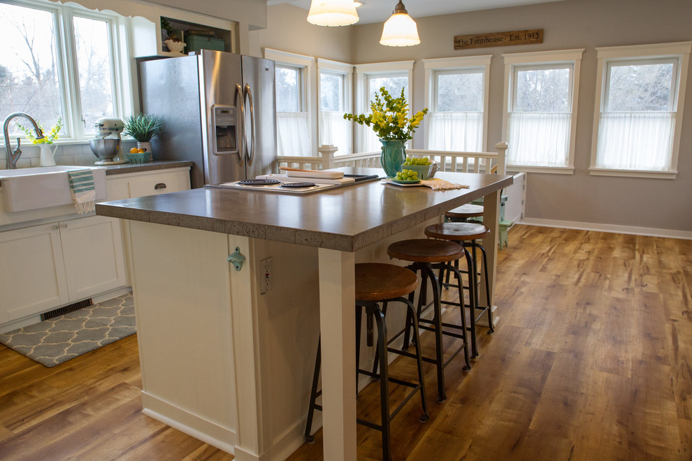 Enclosed kitchen - mid-sized farmhouse l-shaped medium tone wood floor enclosed kitchen idea in Minneapolis with a farmhouse sink, shaker cabinets, white cabinets, concrete countertops, white backsplash, subway tile backsplash, stainless steel appliances and an island