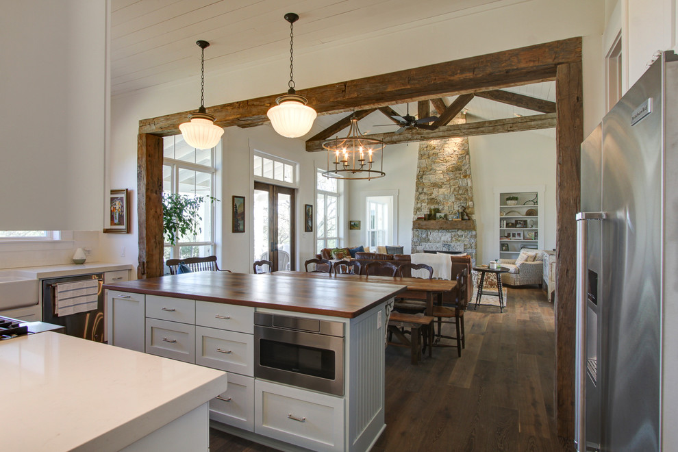 Example of a farmhouse galley medium tone wood floor kitchen design in Austin with a farmhouse sink, flat-panel cabinets, white cabinets, quartzite countertops, white backsplash, porcelain backsplash, stainless steel appliances and an island