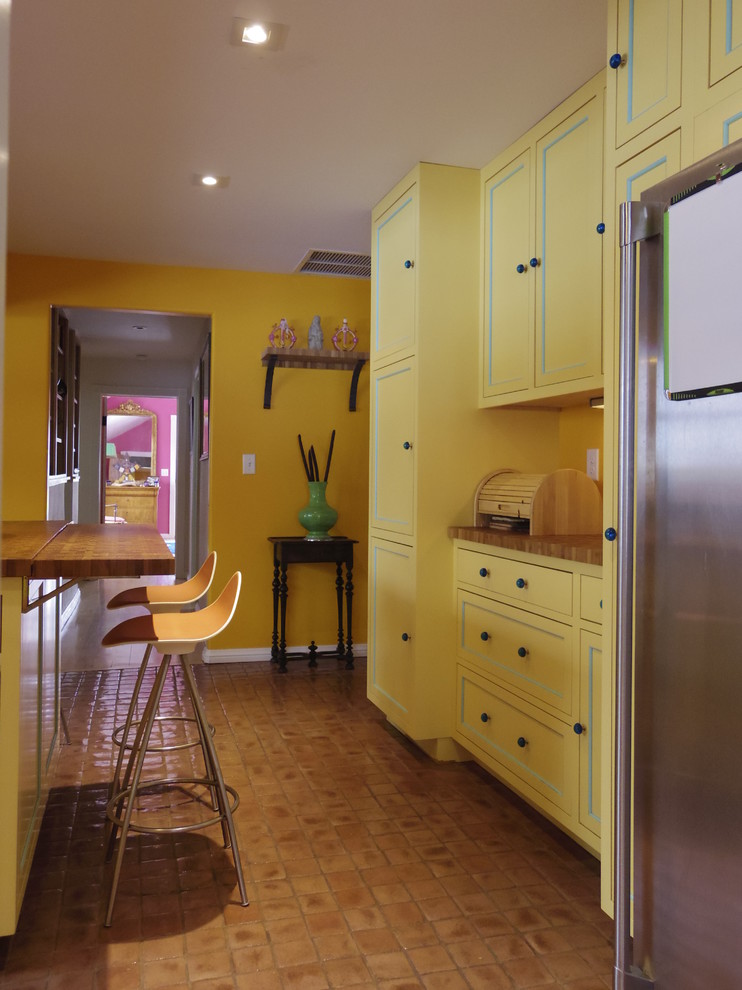 Foto de cocinas en U campestre cerrado con fregadero sobremueble, puertas de armario amarillas, encimera de madera, salpicadero de azulejos tipo metro y electrodomésticos de acero inoxidable