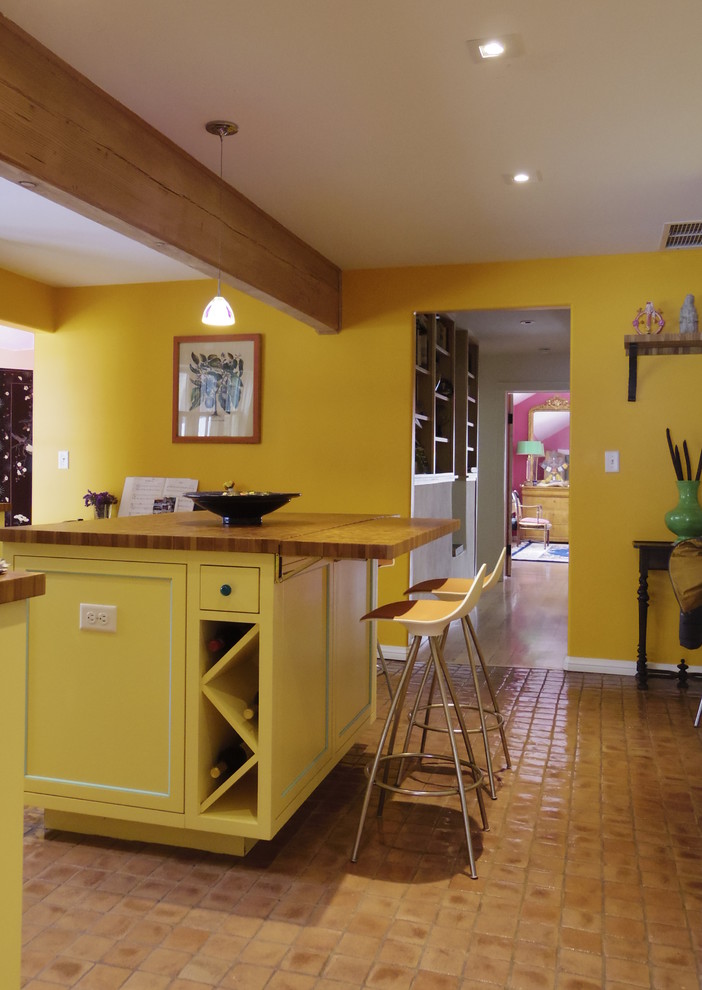 Стильный дизайн: отдельная, п-образная кухня в стиле кантри с желтыми фасадами, с полувстраиваемой мойкой (с передним бортиком), деревянной столешницей, фартуком из плитки кабанчик и техникой из нержавеющей стали - последний тренд