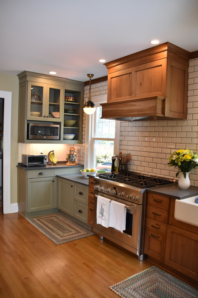 Example of a small country single-wall light wood floor and brown floor enclosed kitchen design in New York with a farmhouse sink, shaker cabinets, medium tone wood cabinets, quartz countertops, white backsplash, subway tile backsplash, stainless steel appliances, gray countertops and an island