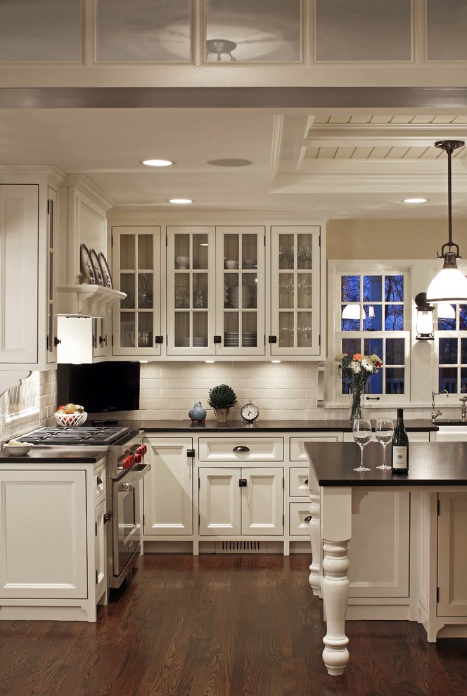 Elegant l-shaped dark wood floor kitchen photo in Omaha with a farmhouse sink, recessed-panel cabinets, white cabinets, white backsplash, subway tile backsplash, stainless steel appliances and an island