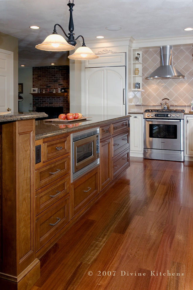 This is an example of a large country u-shaped kitchen/diner in Boston with a belfast sink, beaded cabinets, dark wood cabinets, engineered stone countertops, beige splashback, ceramic splashback, stainless steel appliances, dark hardwood flooring and an island.