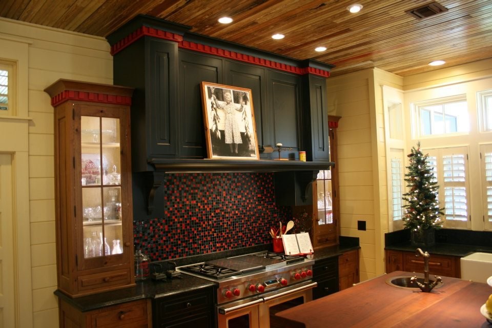 Bild på ett stort lantligt kök, med en rustik diskho, luckor med profilerade fronter, svarta skåp, granitbänkskiva, flerfärgad stänkskydd, stänkskydd i glaskakel, rostfria vitvaror, mellanmörkt trägolv och en köksö