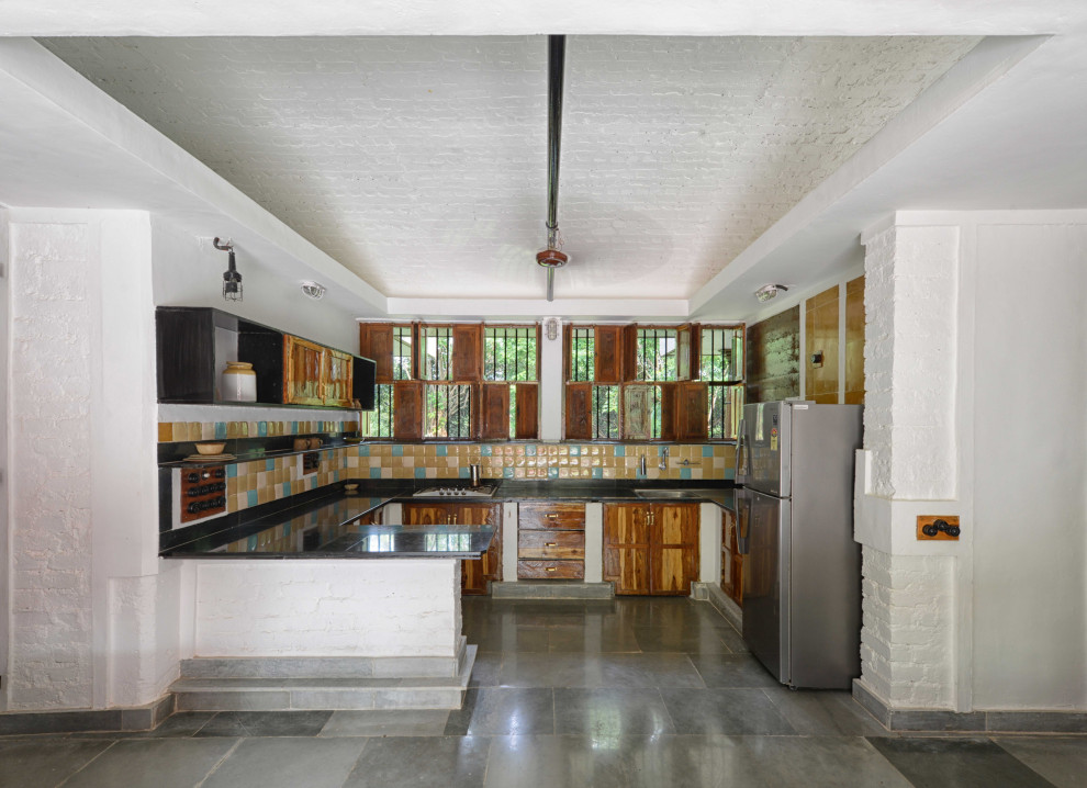 Große Country Küche in U-Form mit Landhausspüle, hellbraunen Holzschränken, Granit-Arbeitsplatte, bunter Rückwand, Rückwand aus Keramikfliesen, Marmorboden, buntem Boden, schwarzer Arbeitsplatte und gewölbter Decke in Mumbai