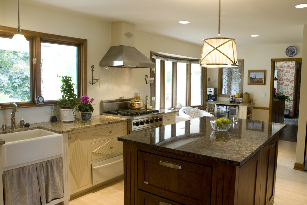 Large traditional u-shaped enclosed kitchen in Minneapolis with stainless steel appliances, a belfast sink, granite worktops, beige cabinets, light hardwood flooring, an island, beige floors and brown worktops.
