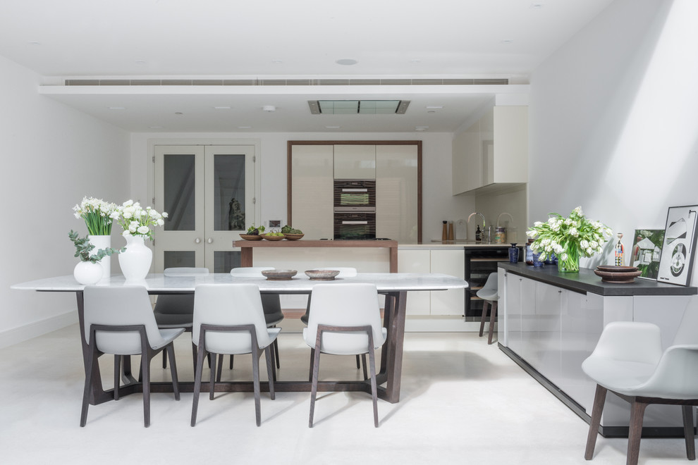 Design ideas for a large contemporary grey and cream kitchen/diner in London with a double-bowl sink, beige cabinets, limestone worktops, beige splashback, glass sheet splashback, integrated appliances and an island.