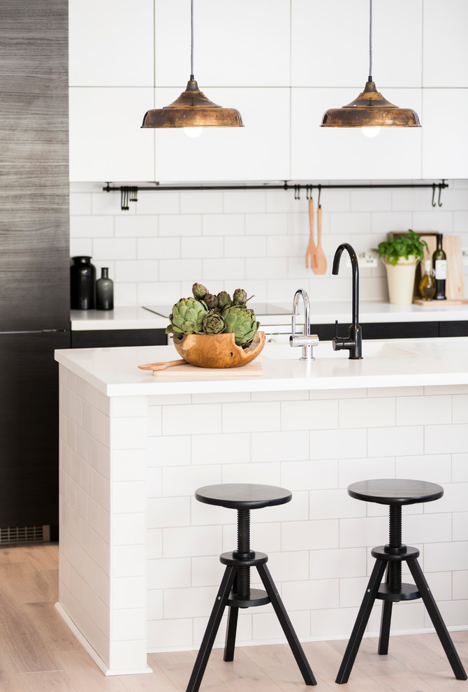 Kitchen - scandinavian light wood floor kitchen idea in London with a drop-in sink, flat-panel cabinets, black cabinets, solid surface countertops, white backsplash, ceramic backsplash and an island