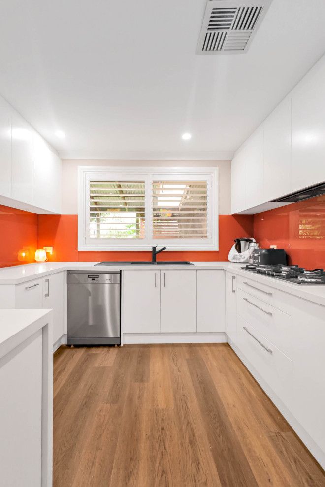 Inspiration for a large modern galley vinyl floor and brown floor open concept kitchen remodel in Sydney with a double-bowl sink, flat-panel cabinets, white cabinets, quartz countertops, orange backsplash, glass sheet backsplash, stainless steel appliances, an island and white countertops