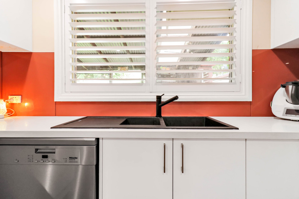Foto på ett stort funkis vit kök, med en dubbel diskho, släta luckor, vita skåp, bänkskiva i kvarts, orange stänkskydd, glaspanel som stänkskydd, rostfria vitvaror, vinylgolv, en köksö och brunt golv