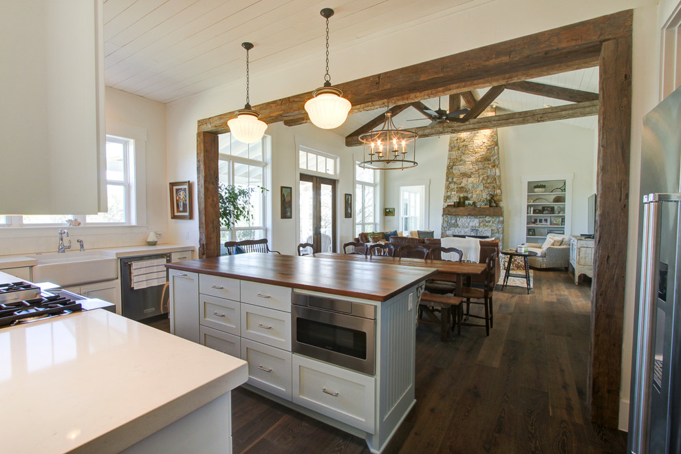 Foto på ett stort lantligt kök, med en rustik diskho, skåp i shakerstil, rostfria vitvaror, en köksö, vita skåp, bänkskiva i kvarts, mörkt trägolv och brunt golv