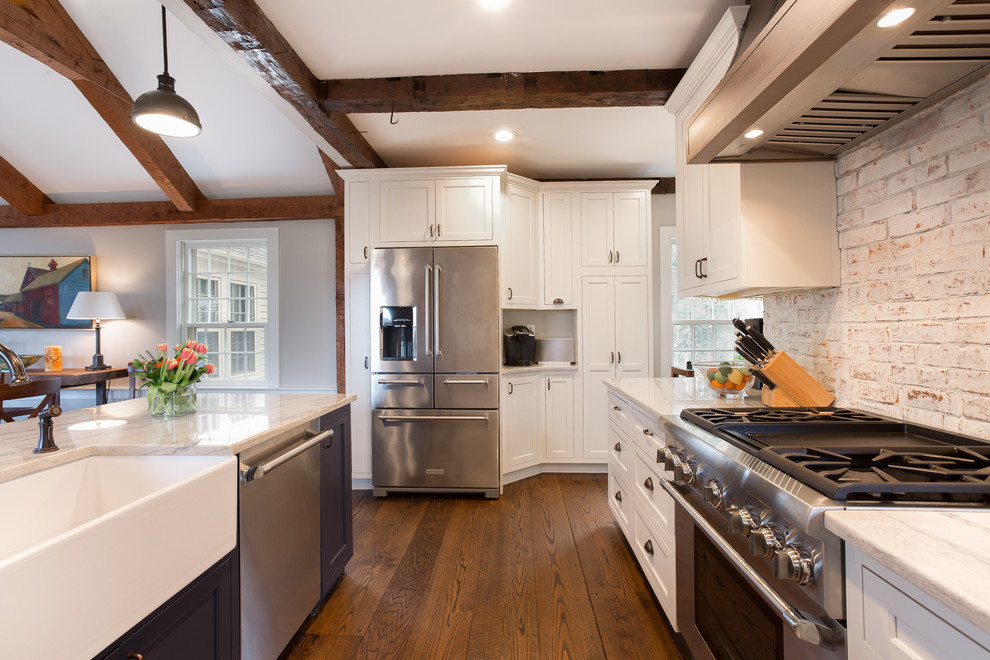 This is an example of a medium sized farmhouse l-shaped open plan kitchen in Providence with a belfast sink, beaded cabinets, white cabinets, quartz worktops, white splashback, brick splashback, stainless steel appliances, medium hardwood flooring and an island.