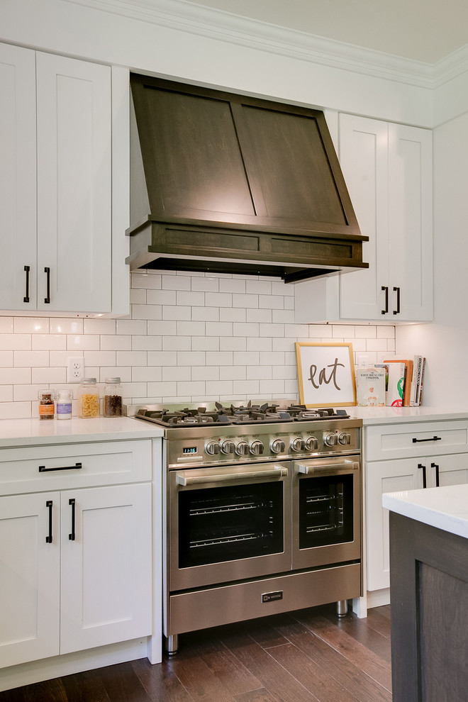 Example of a country u-shaped medium tone wood floor eat-in kitchen design with an undermount sink, shaker cabinets, white cabinets, quartz countertops, white backsplash, subway tile backsplash, stainless steel appliances and an island