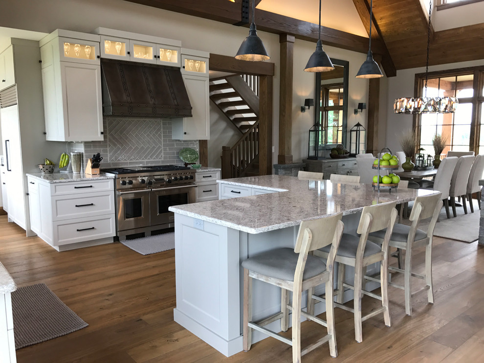 This is an example of an expansive country u-shaped kitchen/diner in Philadelphia with a submerged sink, shaker cabinets, white cabinets, quartz worktops, beige splashback, ceramic splashback, stainless steel appliances, medium hardwood flooring, an island and brown floors.