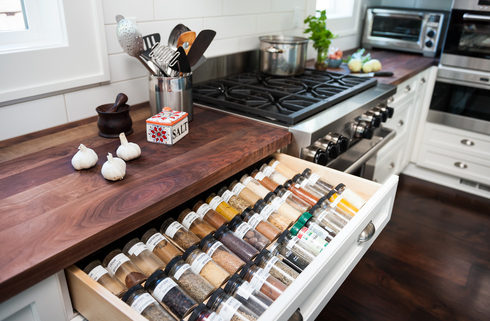 Photo of a medium sized rural l-shaped open plan kitchen in Portland with a belfast sink, flat-panel cabinets, white cabinets, white splashback, ceramic splashback, stainless steel appliances, dark hardwood flooring, an island and wood worktops.