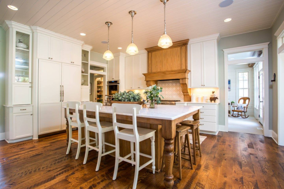 Inspiration for a mid-sized cottage single-wall dark wood floor eat-in kitchen remodel in Minneapolis with recessed-panel cabinets, an island, white cabinets, marble countertops, white backsplash, ceramic backsplash, a farmhouse sink and paneled appliances