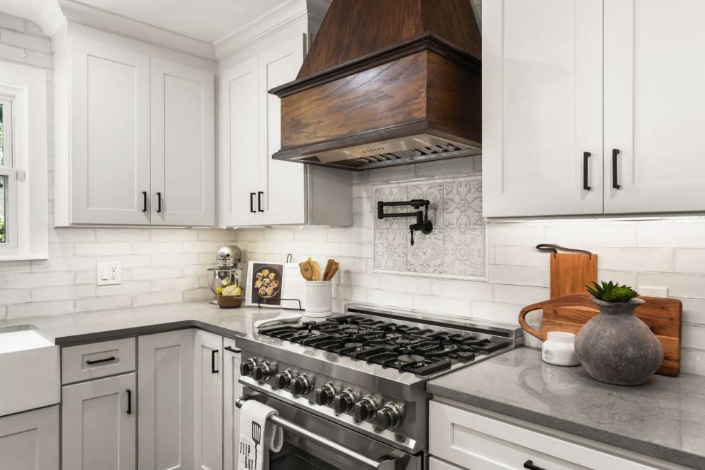 Example of a country l-shaped ceramic tile eat-in kitchen design in Jacksonville with a farmhouse sink, shaker cabinets, white cabinets, quartz countertops, white backsplash, stainless steel appliances and an island