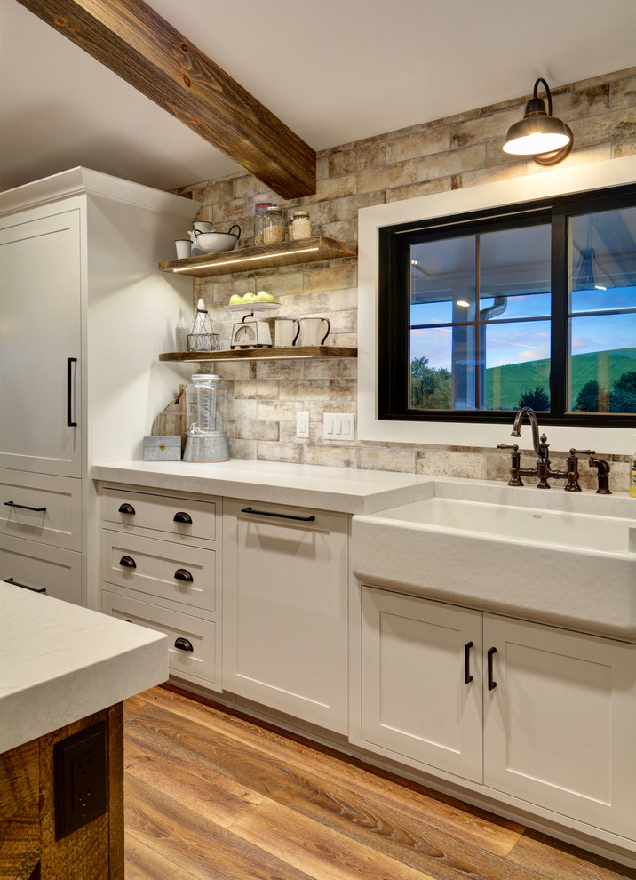 Farmhouse l-shaped medium tone wood floor and brown floor open concept kitchen photo in Chicago with a farmhouse sink, raised-panel cabinets, distressed cabinets, multicolored backsplash, ceramic backsplash, stainless steel appliances, an island and white countertops