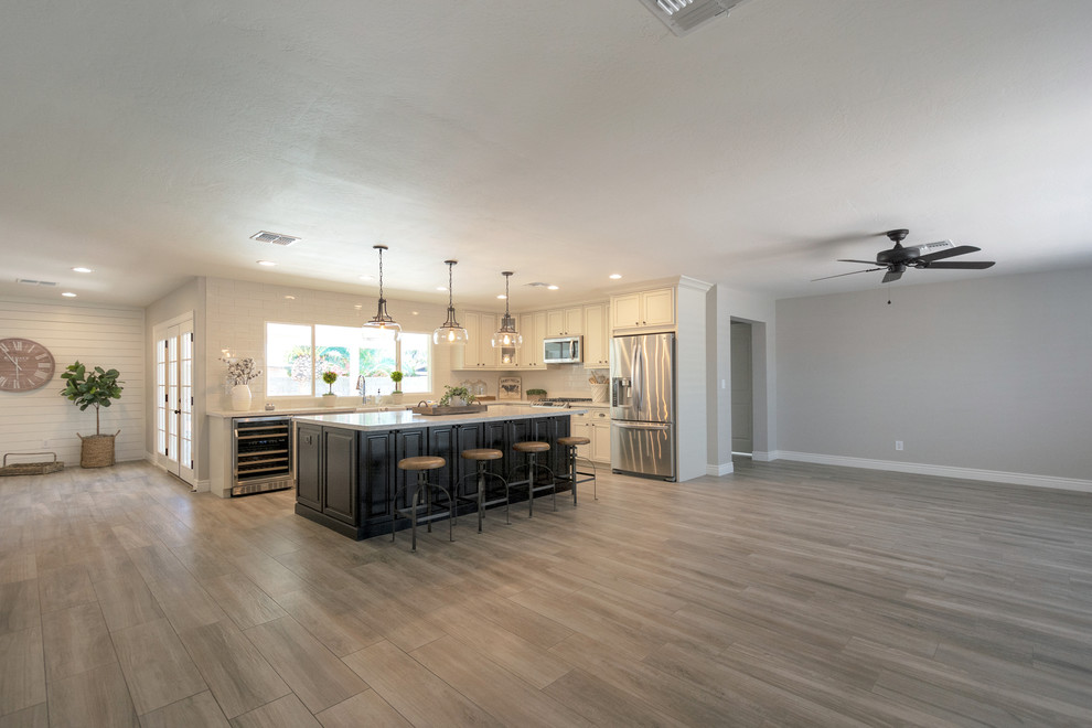 Example of a large country l-shaped porcelain tile and brown floor open concept kitchen design in Phoenix with a farmhouse sink, recessed-panel cabinets, white cabinets, quartz countertops, white backsplash, subway tile backsplash, stainless steel appliances, an island and white countertops
