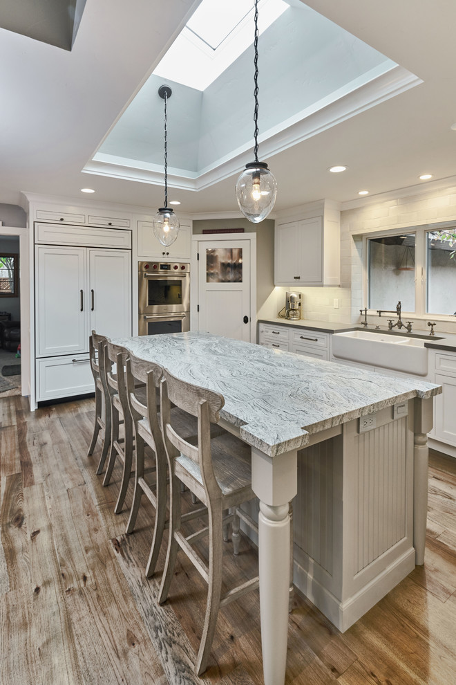 Inspiration for a large farmhouse u-shaped light wood floor open concept kitchen remodel in San Francisco with a farmhouse sink, beaded inset cabinets, white cabinets, granite countertops, gray backsplash, stone tile backsplash, paneled appliances and an island